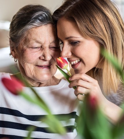 Seniorin und Betreuerin riechen an einer Tulpe