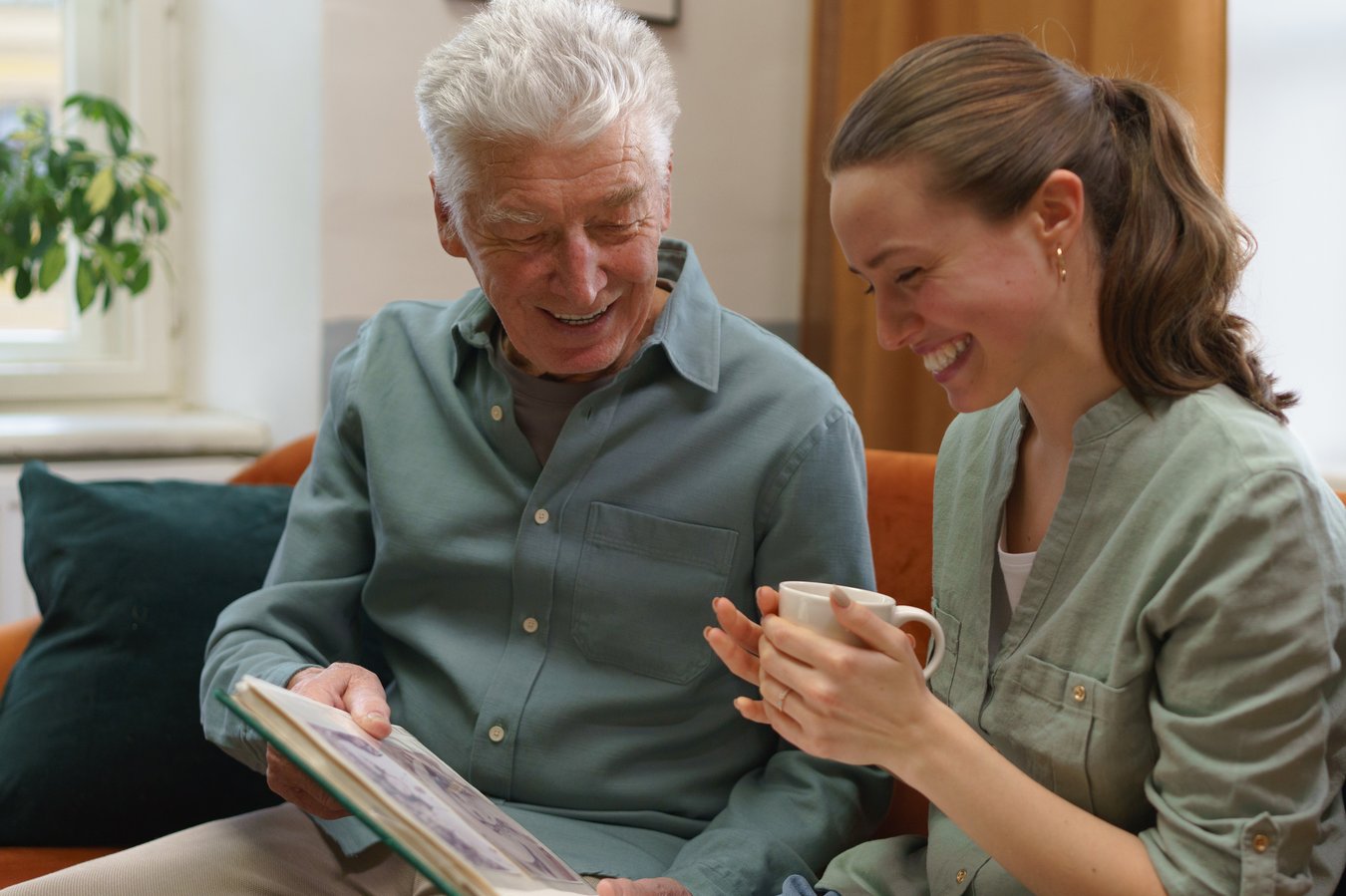 Senior und ehrenamtliche Helferin schauen gemeinsam ein Fotoalbum an.